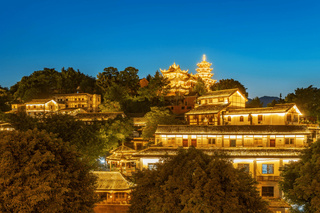 Traditional buildings lit up on a wooded hillside at dusk, Chongqing