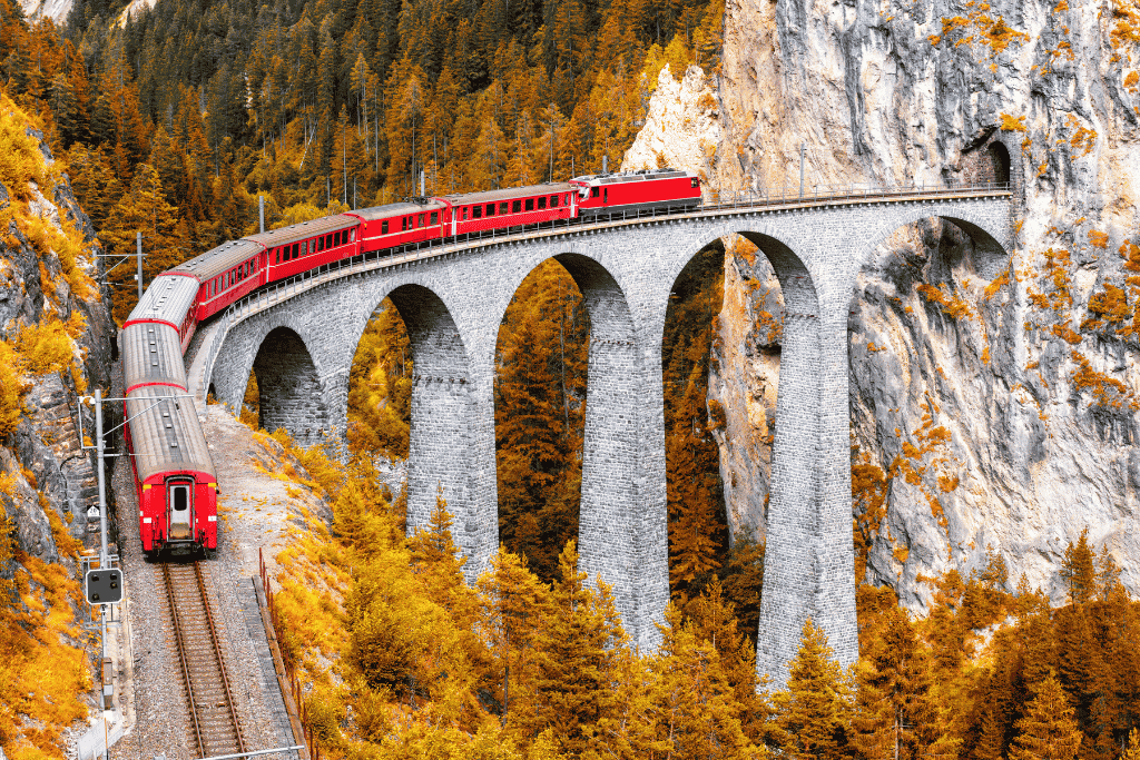 A red train crossing the arched Landwasser Viaduct through golden autumn larch forest
