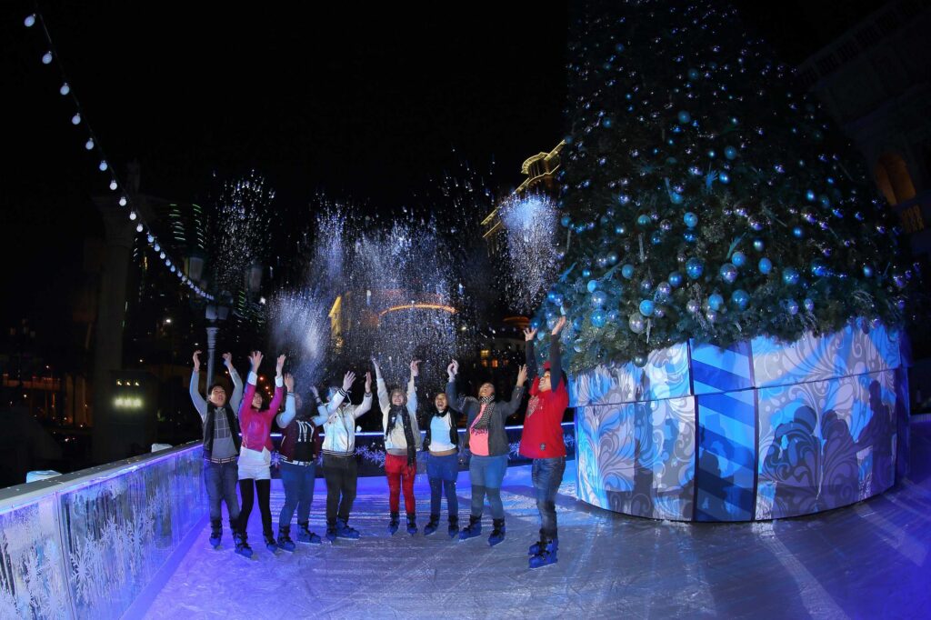 People ice skating outdoors at night beside a large decorated Christmas tree and fairy lights