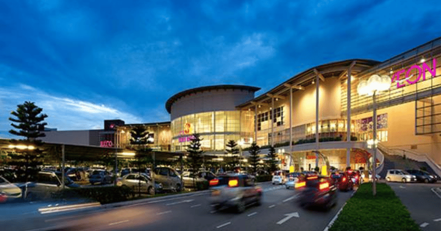 AEON Mall Bukit Indah lit up at dusk, its curved glass facade and AEON sign above the car park