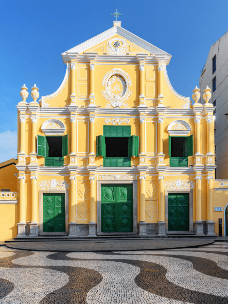 The yellow baroque facade of St. Dominic's Church with green shutters and wave-patterned paving in Macau