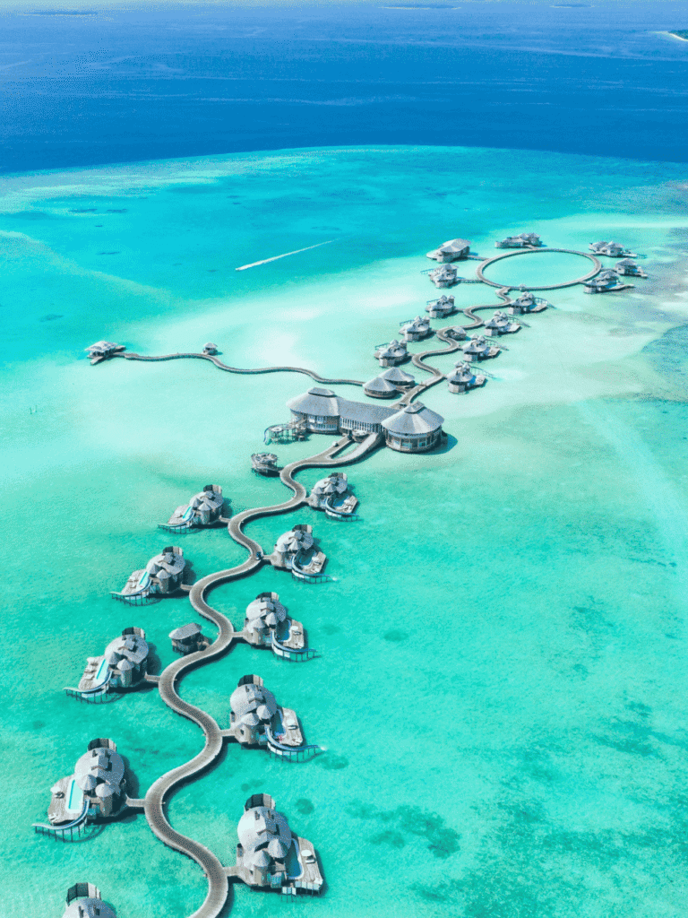 Aerial view of a Maldives resort's overwater villas linked by a winding jetty over a turquoise lagoon