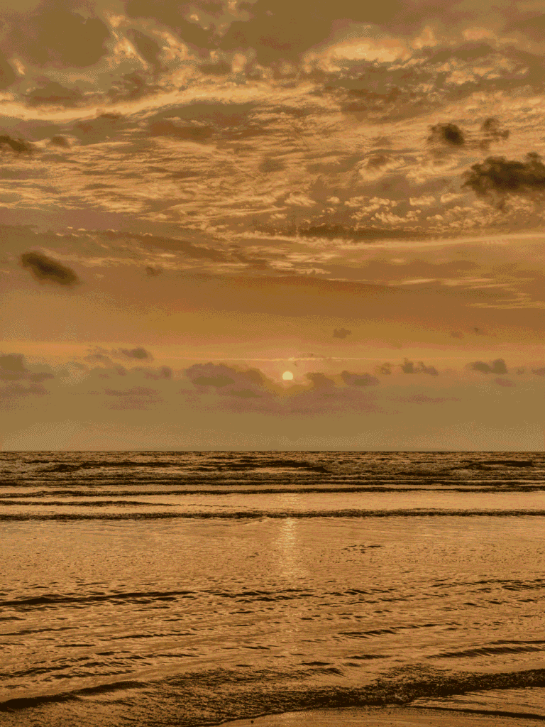 Waves rolling onto a wide, empty Desaru beach under a golden sunset