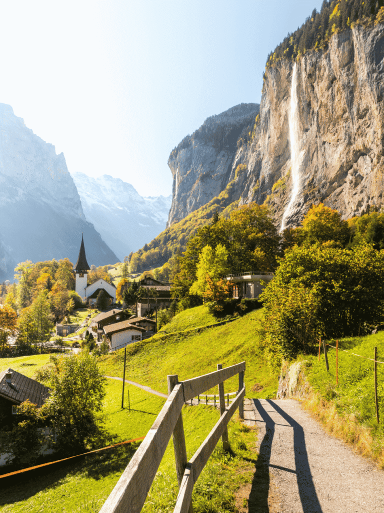 A path past a village church toward a waterfall falling down the cliffs of Lauterbrunnen