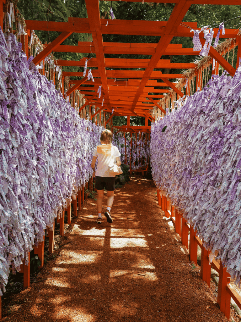 A visitor walking a corridor lined with tied paper fortune slips under red wooden frames