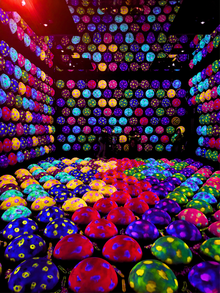 Dark room filled with glowing multicoloured polka-dot spheres on the floor and walls at teamLab