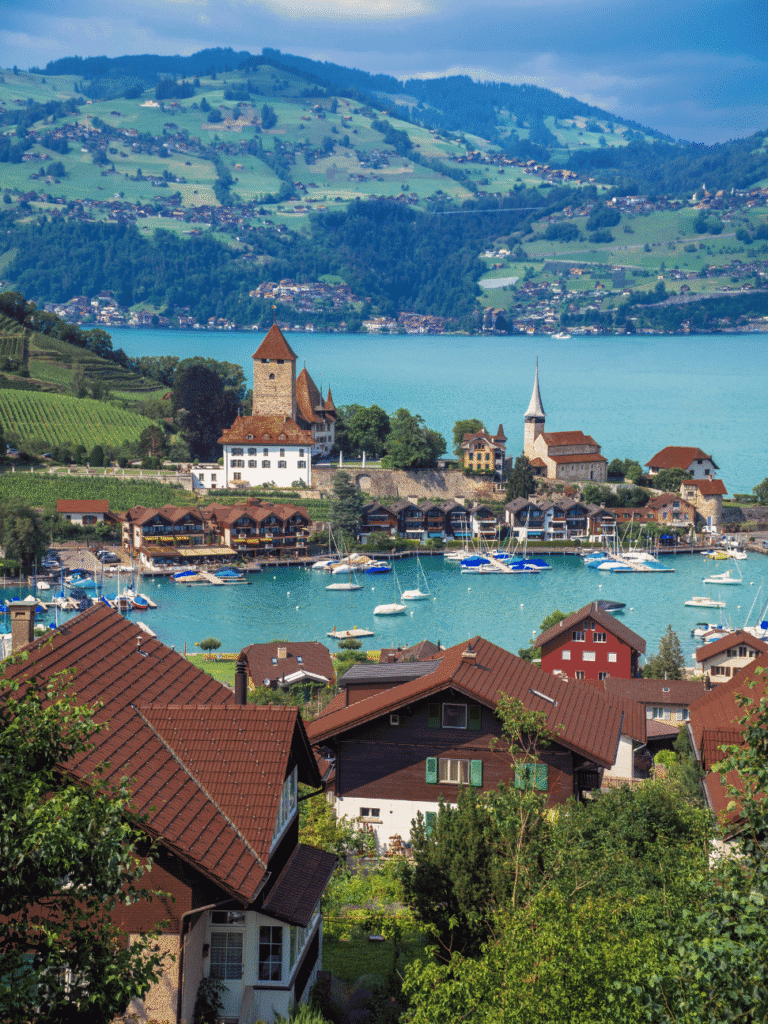 Sailboats moored below a lakeside castle and church on the turquoise shore of Lake Thun