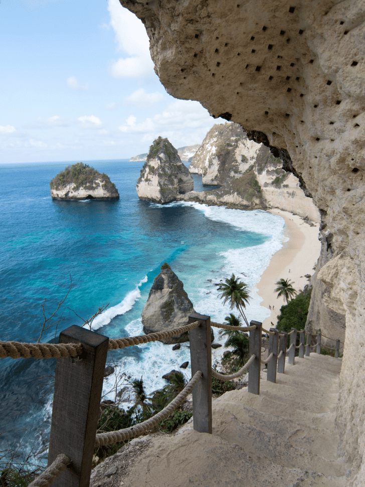 Rope-railed stone stairway descending to Atuh Beach past limestone pinnacles and turquoise bay