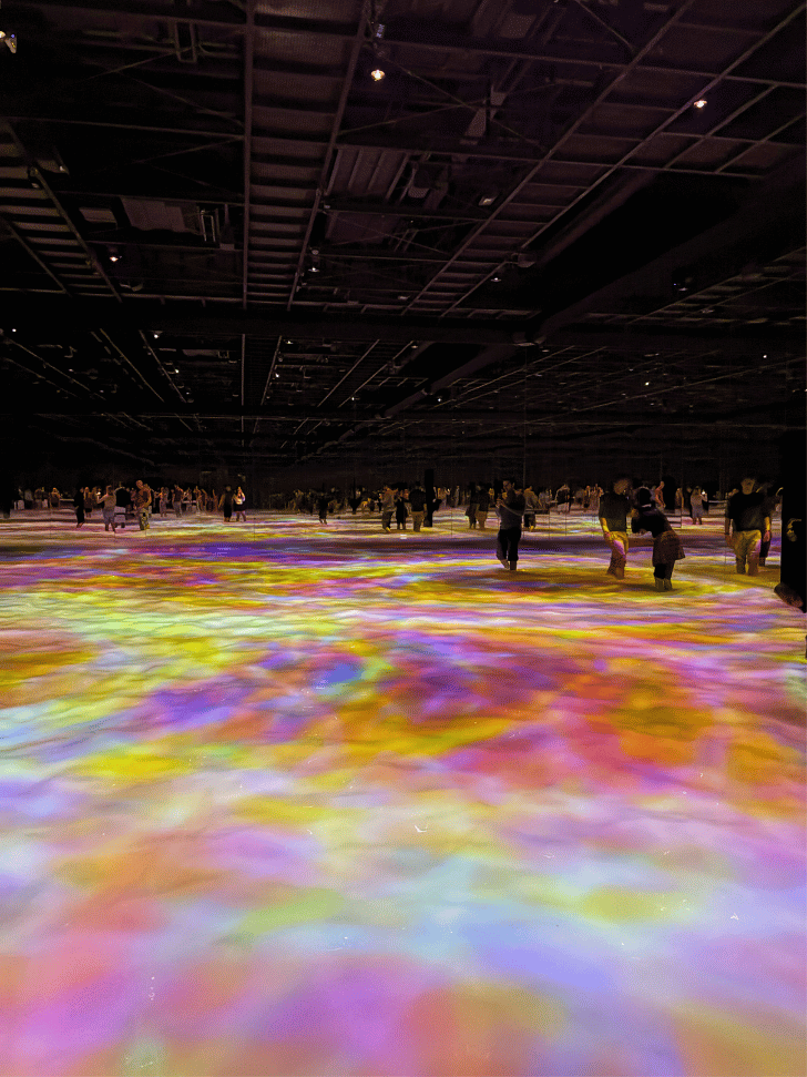 Visitors wading through a glowing pink and yellow projected water floor at teamLab Planets