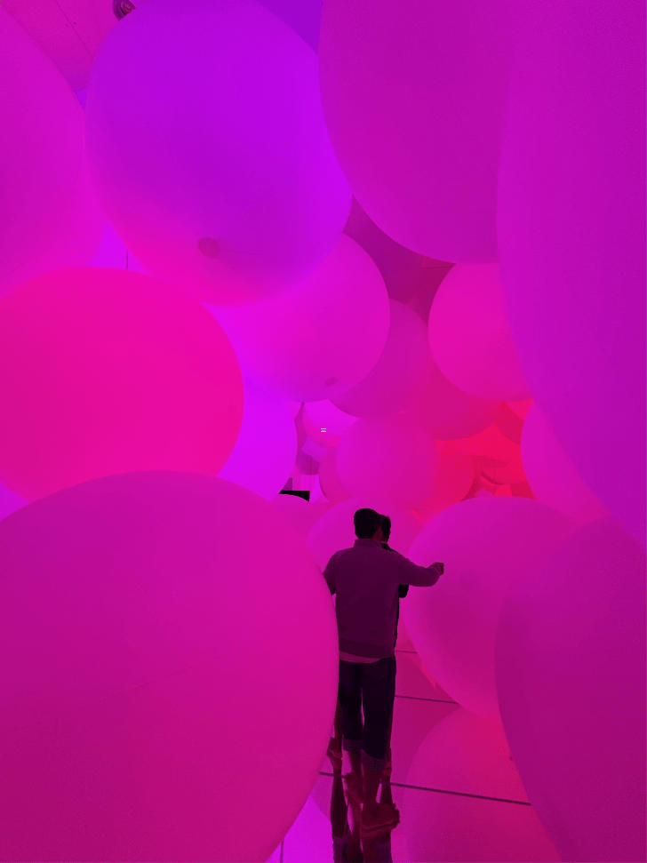 Visitor pushing a giant glowing pink sphere among many floating spheres at teamLab