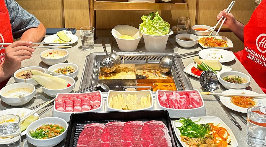 Haidilao hotpot table with a divided broth pot and platters of sliced meat and vegetables