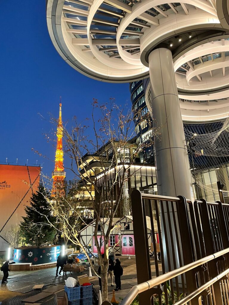 Tokyo Tower lit orange at dusk beside the curved white canopy of Azabudai Hills