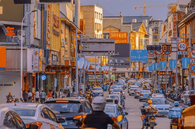 A busy Zhangjiajie city street at dusk with cars, taxis and scooters