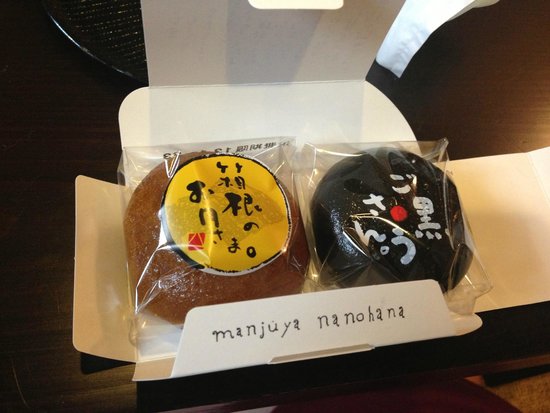 Two steamed onsen manju buns, one pale and one black sesame, in a Nanohana box
