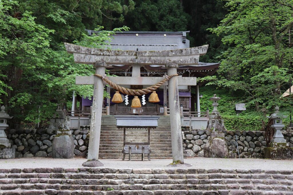 Stone torii gate with a straw rope and the forested approach to Shirakawa Hachiman Shrine