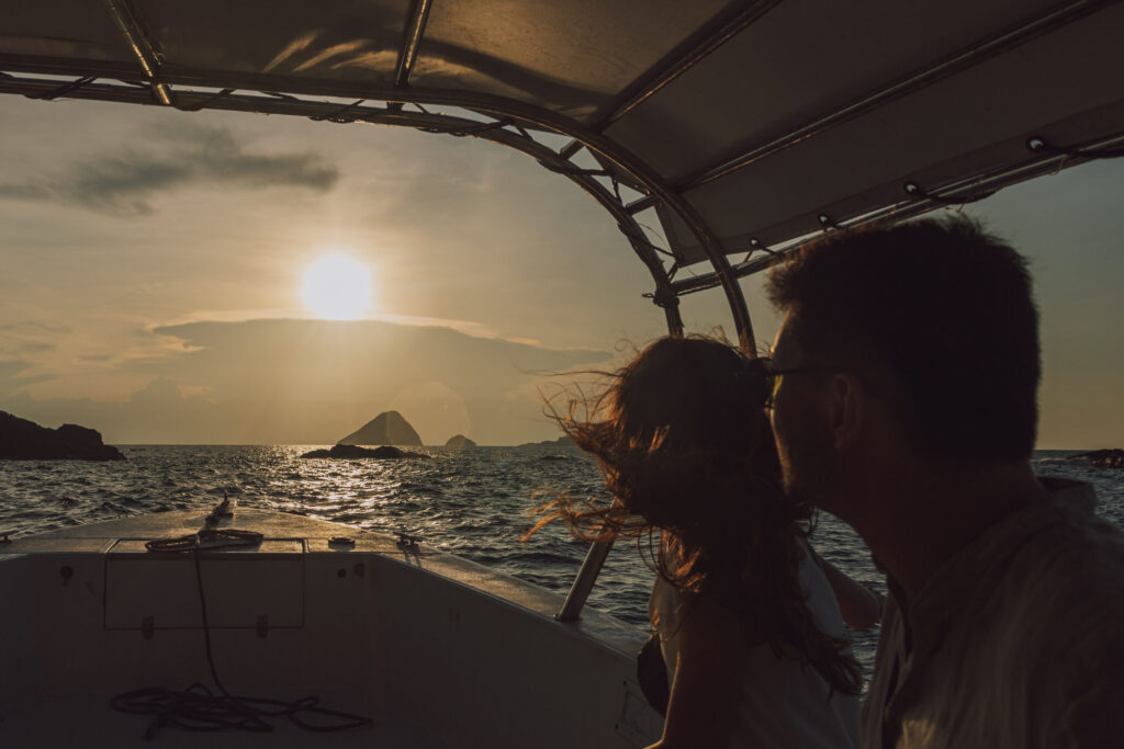 A couple on a boat watching the sun set over the sea and rocky islets in the Perhentians