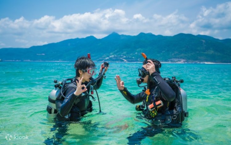 Two scuba divers in full gear standing in shallow turquoise water before a dive