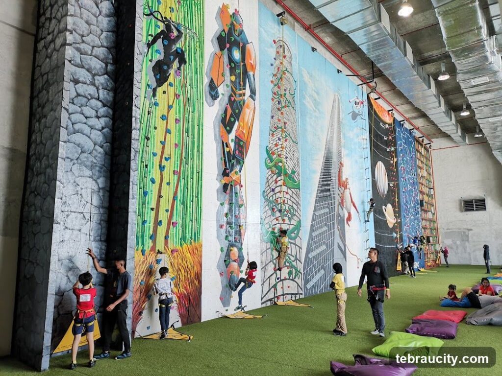 Children climbing tall, mural-painted walls with harnesses at an indoor rock-climbing gym
