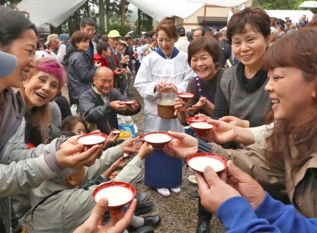 Festival-goers smiling and toasting with red lacquer cups of milky doburoku sake
