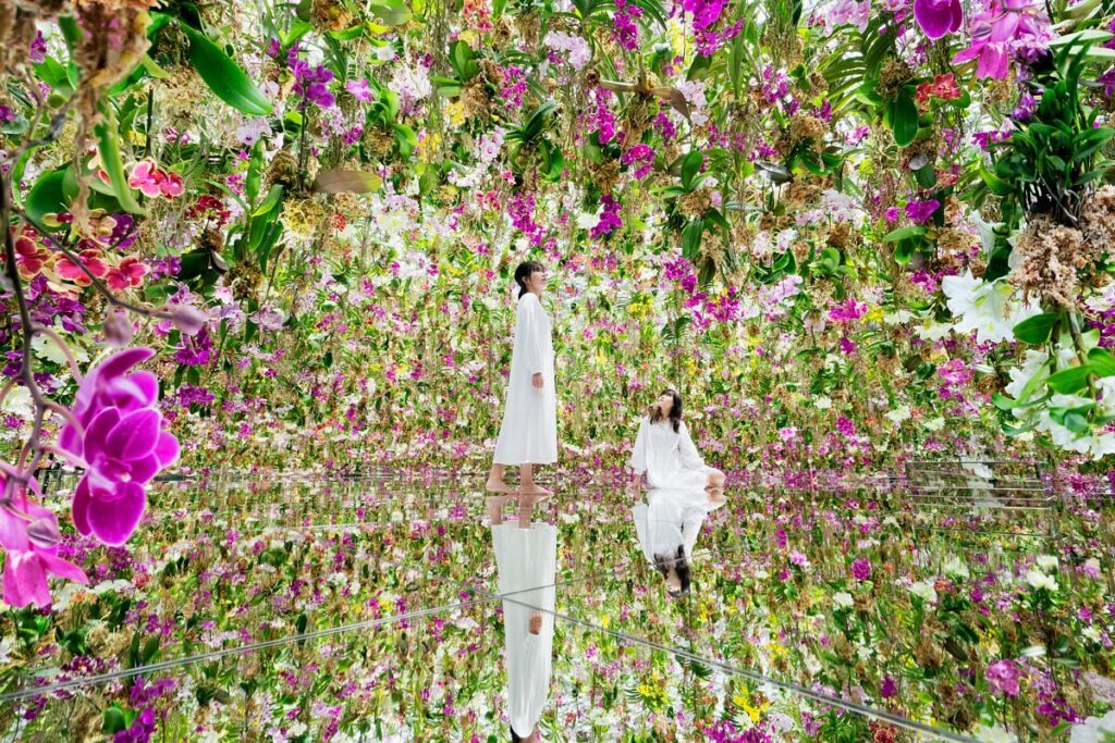 Visitor surrounded by thousands of hanging orchids reflected on a mirror floor in the Floating Flower Garden