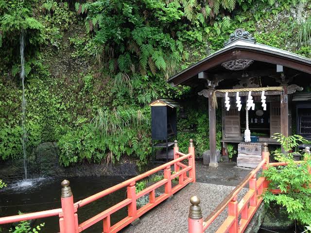 A small shrine with a red bridge beside a waterfall and mossy cliff at Zeniarai Benten, Kamakura
