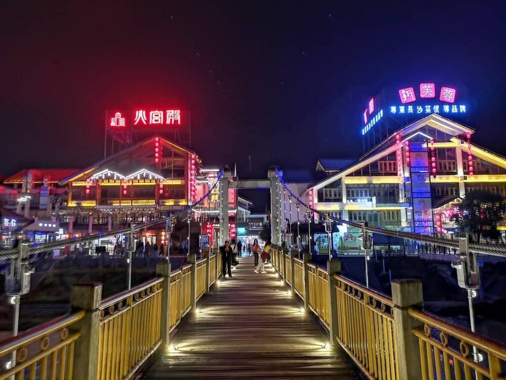 A lit pedestrian bridge and neon-lit riverside buildings at Xibu Street after dark
