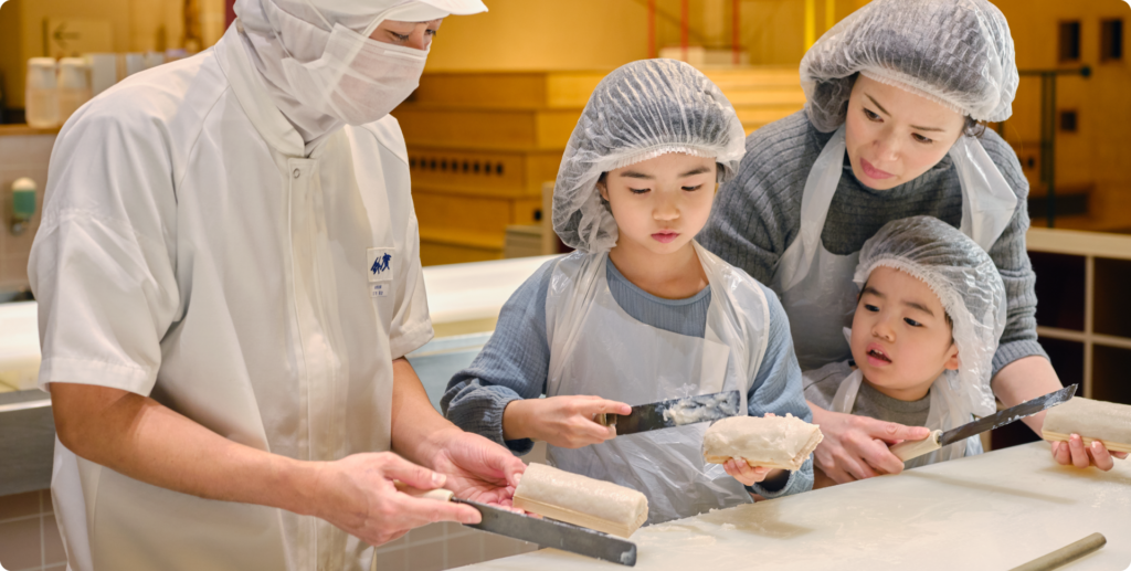 A family in hairnets and aprons shaping white fish paste with a staff member's help