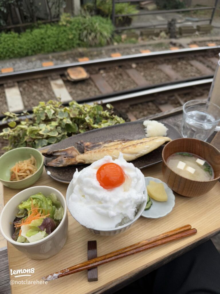 A grilled-fish set meal with rice, egg and miso soup on a tray beside the Enoden tracks at Cafe Yoridokoro