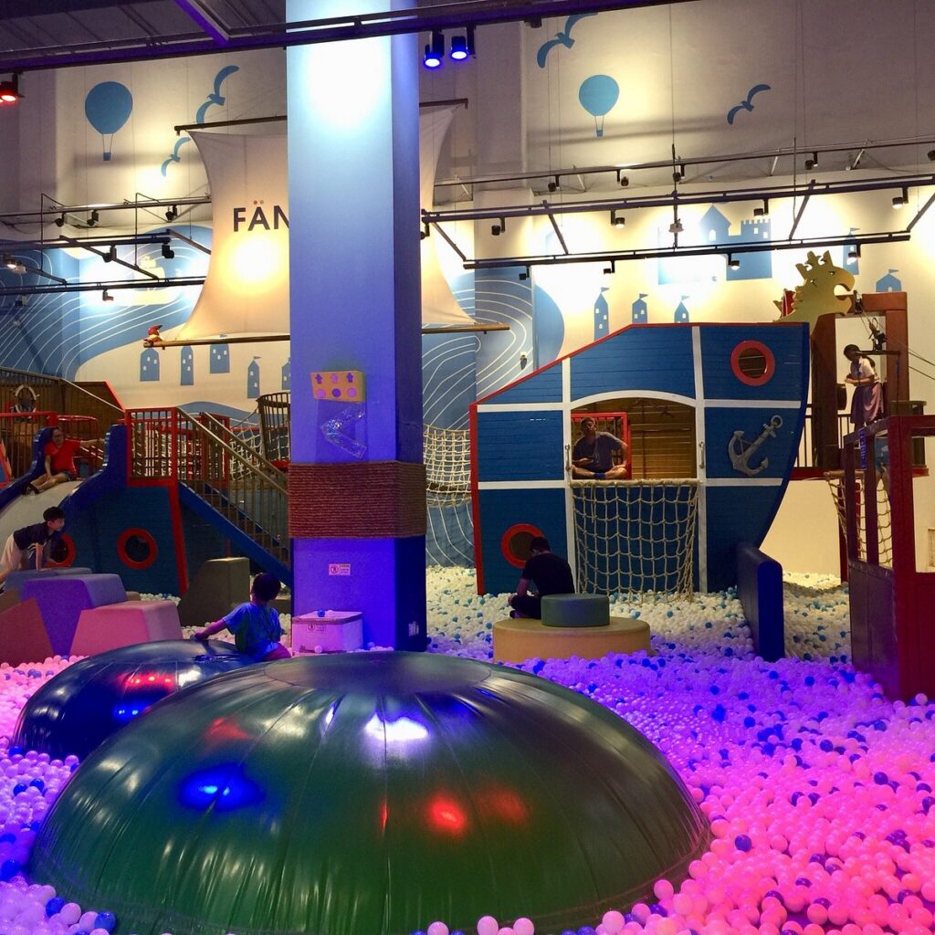 Children playing in a colourful ball pit and pirate-ship play structure at an indoor playground