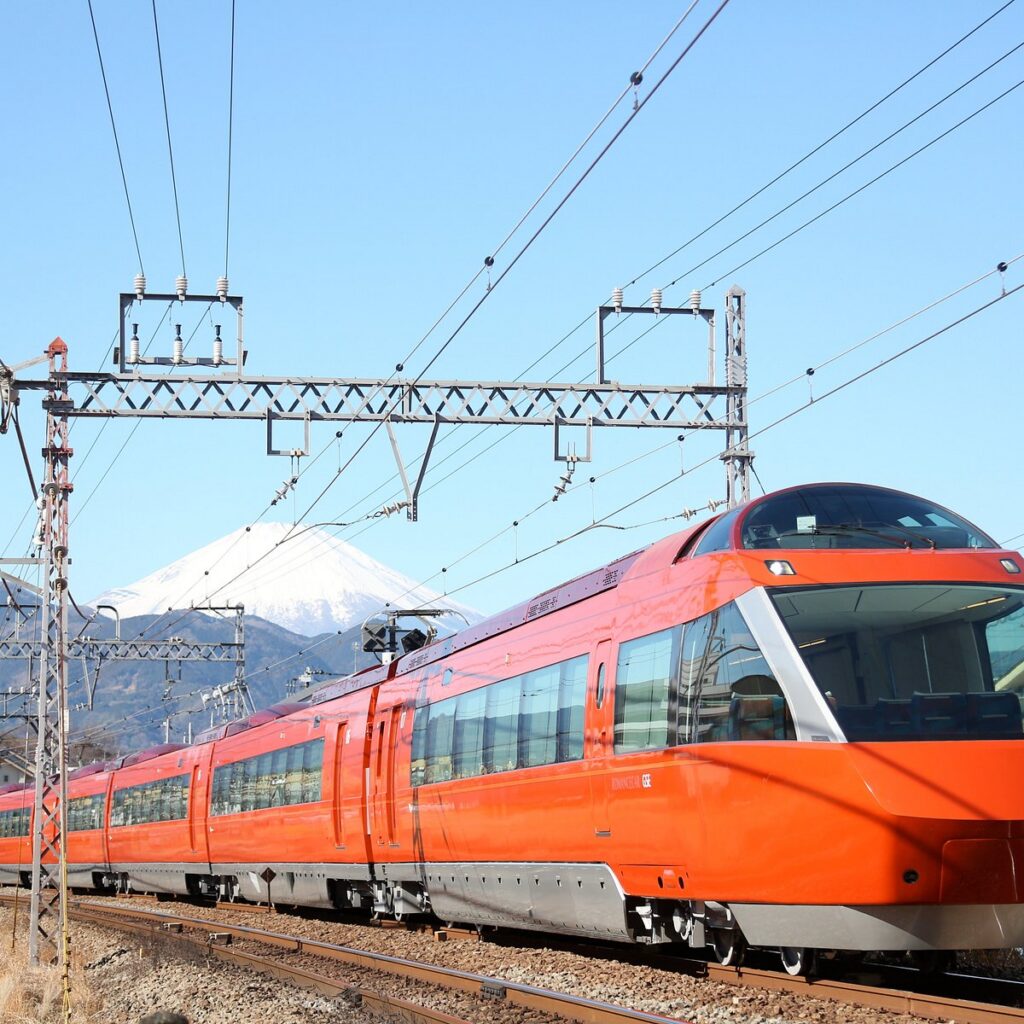 The orange Odakyu Romancecar limited express train running past a snow-capped Mt Fuji