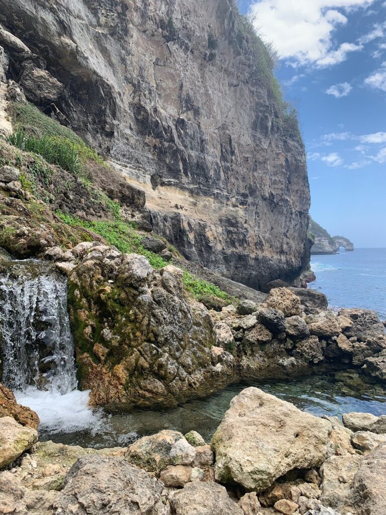 A small waterfall spilling into a rock pool beneath towering sea cliffs at Seganing