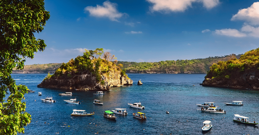 Snorkel and dive boats moored around the small forested islet in Crystal Bay, Nusa Penida