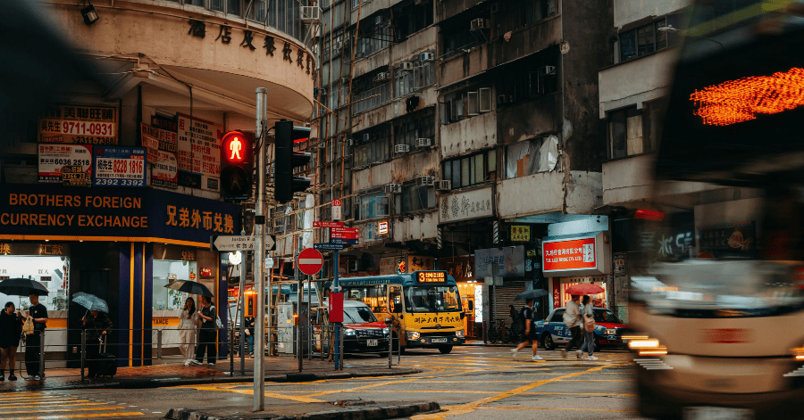 A busy Hong Kong street at dusk with a currency-exchange shopfront, minibus and neon signs