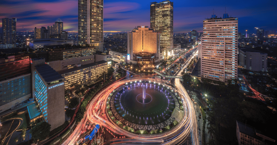 Jakarta's floodlit roundabout fountain amid skyscrapers with traffic light trails at night