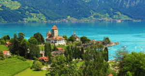 A lakeside castle and church above the turquoise water of Lake Thun, mountains behind