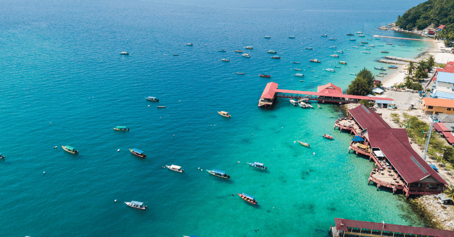 Aerial view of Perhentian Kecil's bay dotted with boats beside red-roofed jetty buildings and a beach