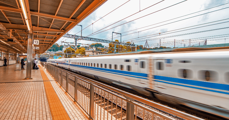 A blue and white bullet train speeding past a covered station platform