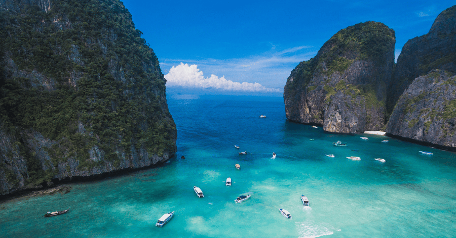 Aerial view of speedboats anchored in a turquoise bay enclosed by limestone cliffs