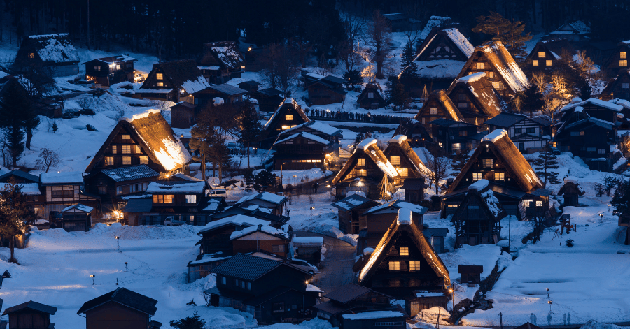 Snow-covered gassho-zukuri houses glowing warmly at night in Shirakawago