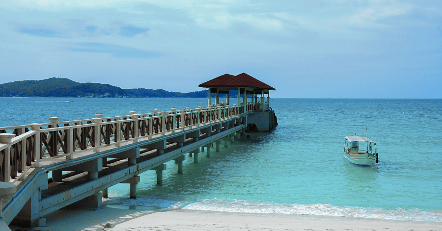 Wooden jetty with a red-roofed pavilion reaching over clear turquoise water at the Perhentian Islands