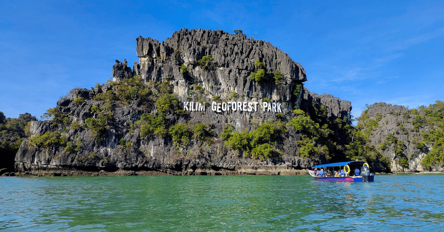 Tour boat passing a karst outcrop marked Kilim Geoforest Park, Langkawi