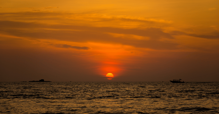Orange sun setting over the sea with a boat off Pantai Cenang, Langkawi