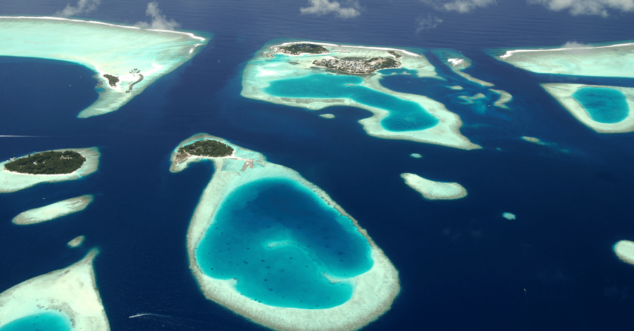 Aerial view of several Maldives coral atolls, turquoise lagoons ringed by reef in deep blue ocean