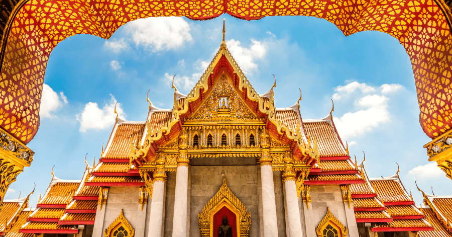 Ornate golden-roofed Thai temple framed by a gilded arch under a blue sky