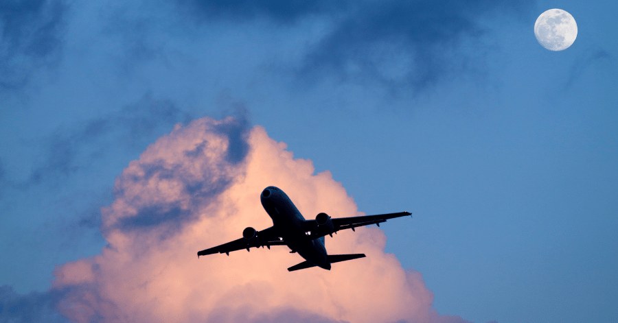 Passenger plane silhouetted against a dusk sky with a full moon