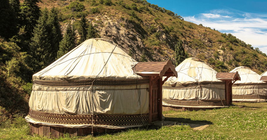 Felt yurts with decorated trim set in a green mountain valley