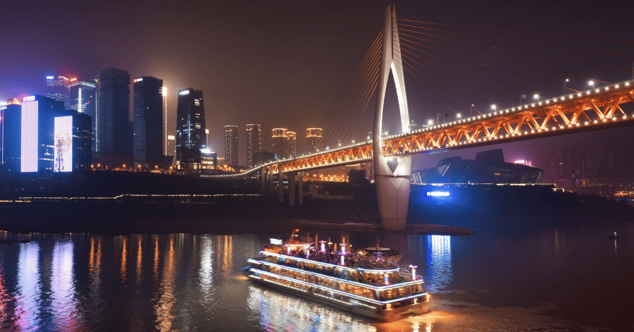 A lit night-cruise boat passing the bridge and skyline, Chongqing