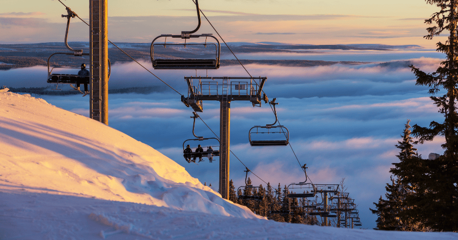 An empty ski chairlift climbing a snowy slope above a sea of cloud at sunrise