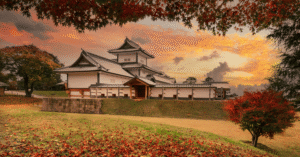 Kanazawa Castle's white turret behind red autumn maple leaves at sunset
