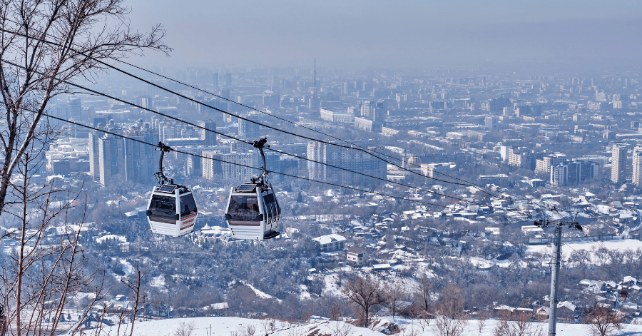 Two cable-car gondolas gliding over a snow-covered Almaty in winter
